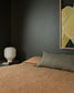 Bedroom with brown bedding, gray pillow, and abstract art on a dark wall.