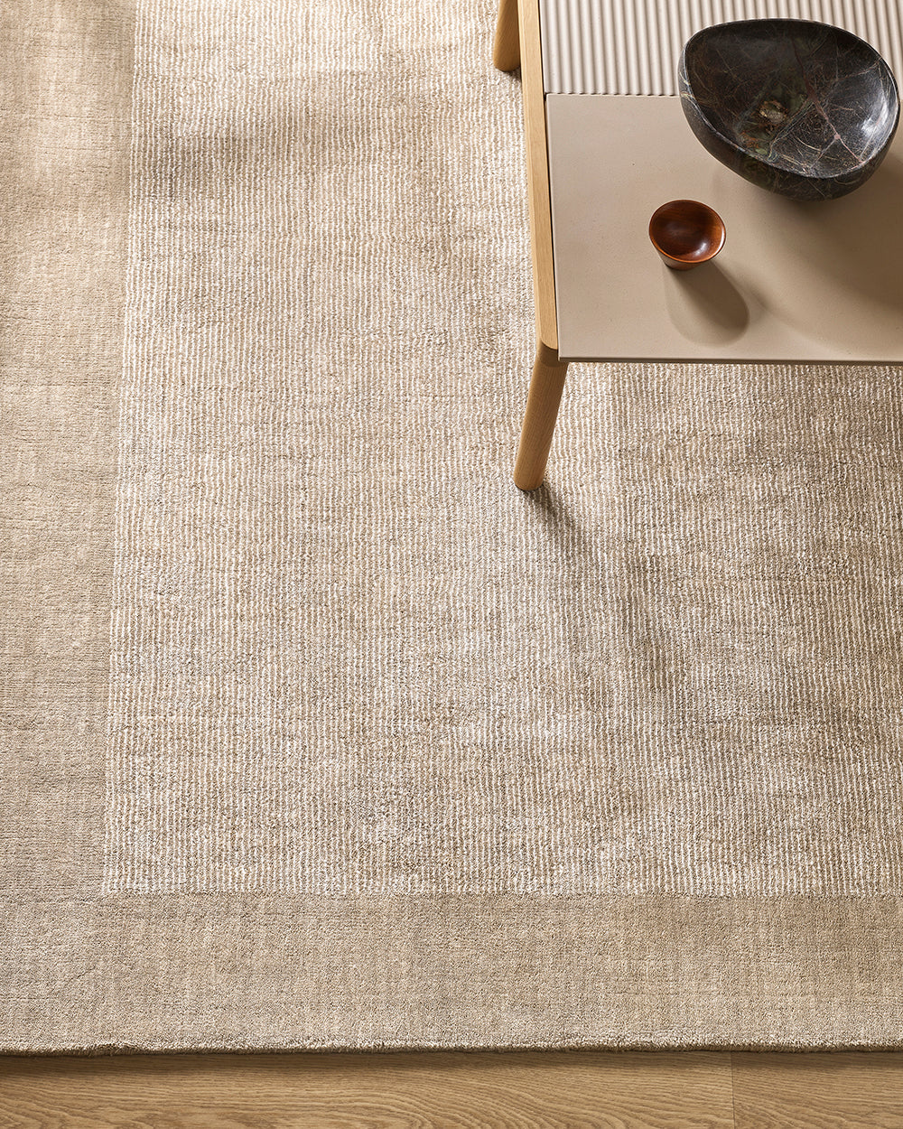 Textured beige rug with a wooden table and decorative bowls on a wooden floor.