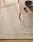 Textured beige rug with a wooden table and decorative bowls on a wooden floor.