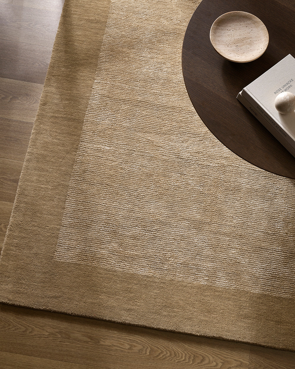 Textured beige rug on a wooden floor with a dark round table and small bowl.
