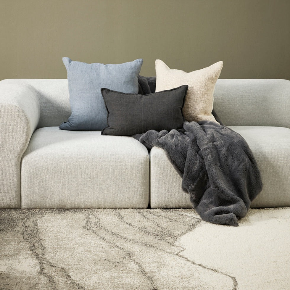 Cloud blue, ecru and charcoal cushions sitting on a whitel modern sofa with sage green walls and cream patterned rug