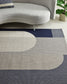 Gray and blue patterned rug in a living room setting with a sofa and plant.