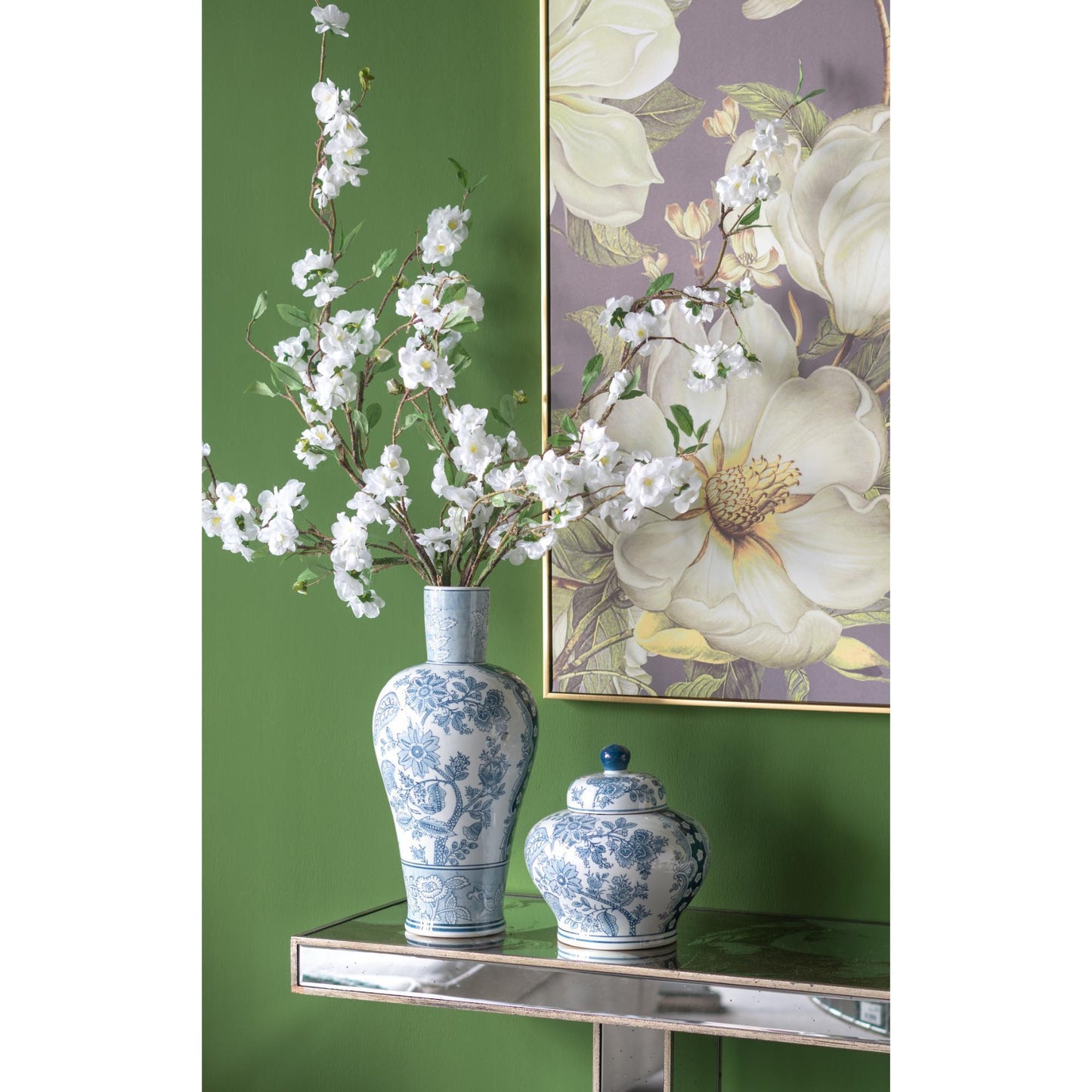 Decorative vases with floral design on a green wall with a floral painting.