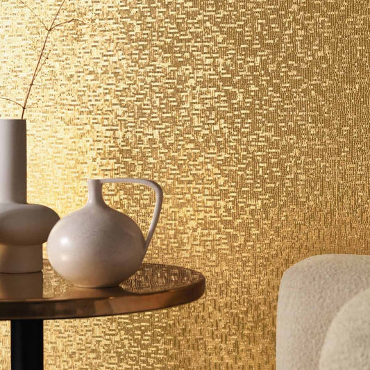 Decorative wall with textured gold pattern, table with white vase, and beige chair.