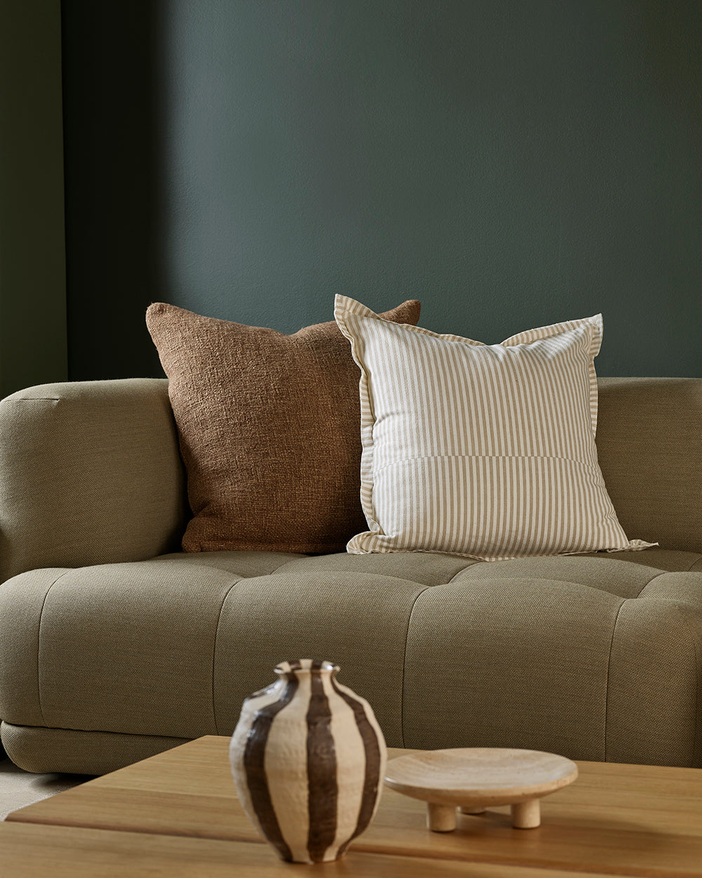 Gray sofa with two pillows and a decorative vase on a wooden table in a room.