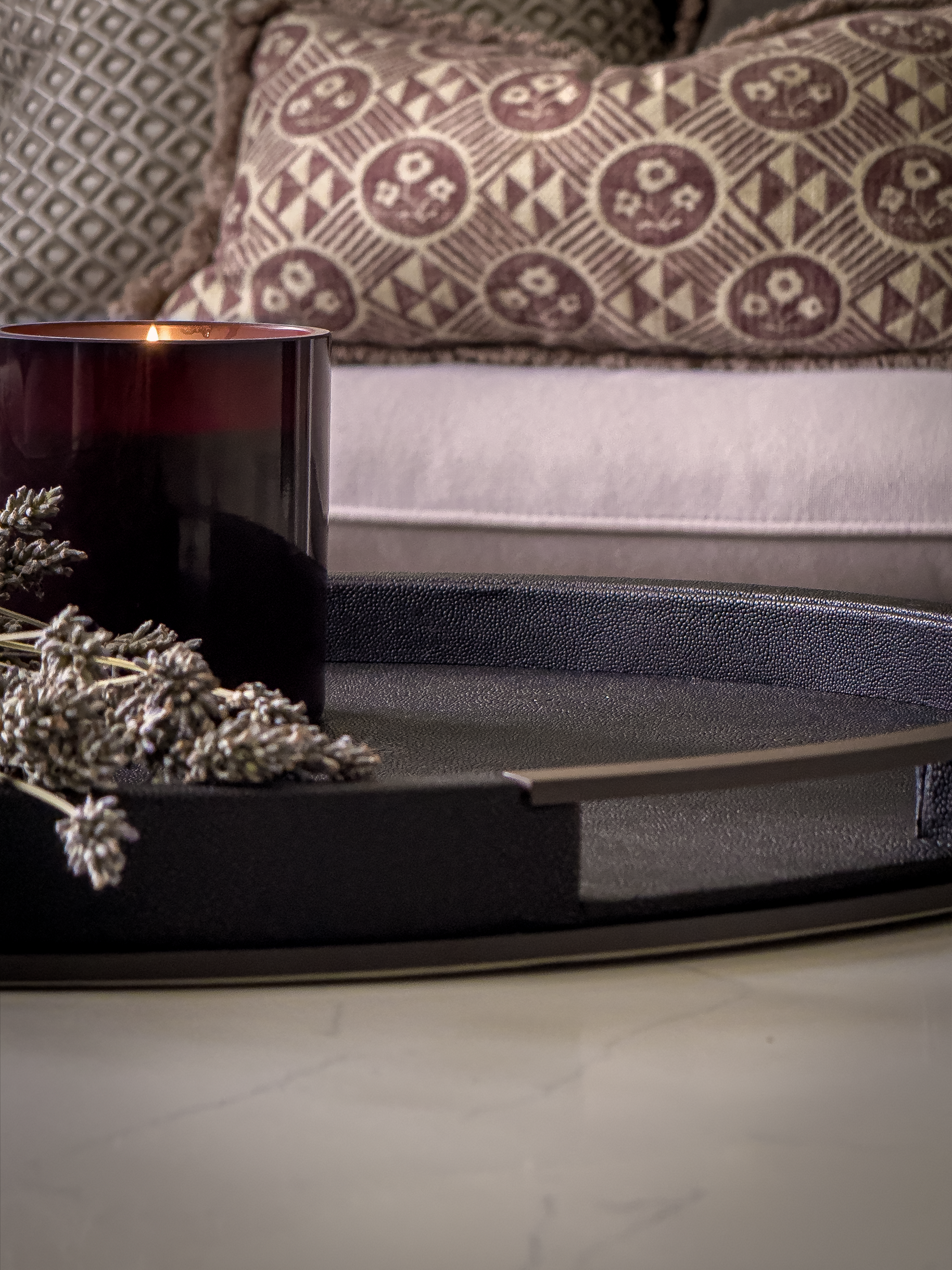 Candle and lavender on a shagreen tray with a patterned pillow in the background