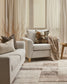Cozy living room with beige sofa and armchair, decorative pillows, and a wooden side table.