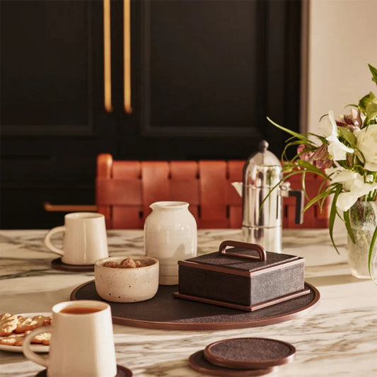 Table setting with coffee cups, a teapot, and a small box on a marble surface.