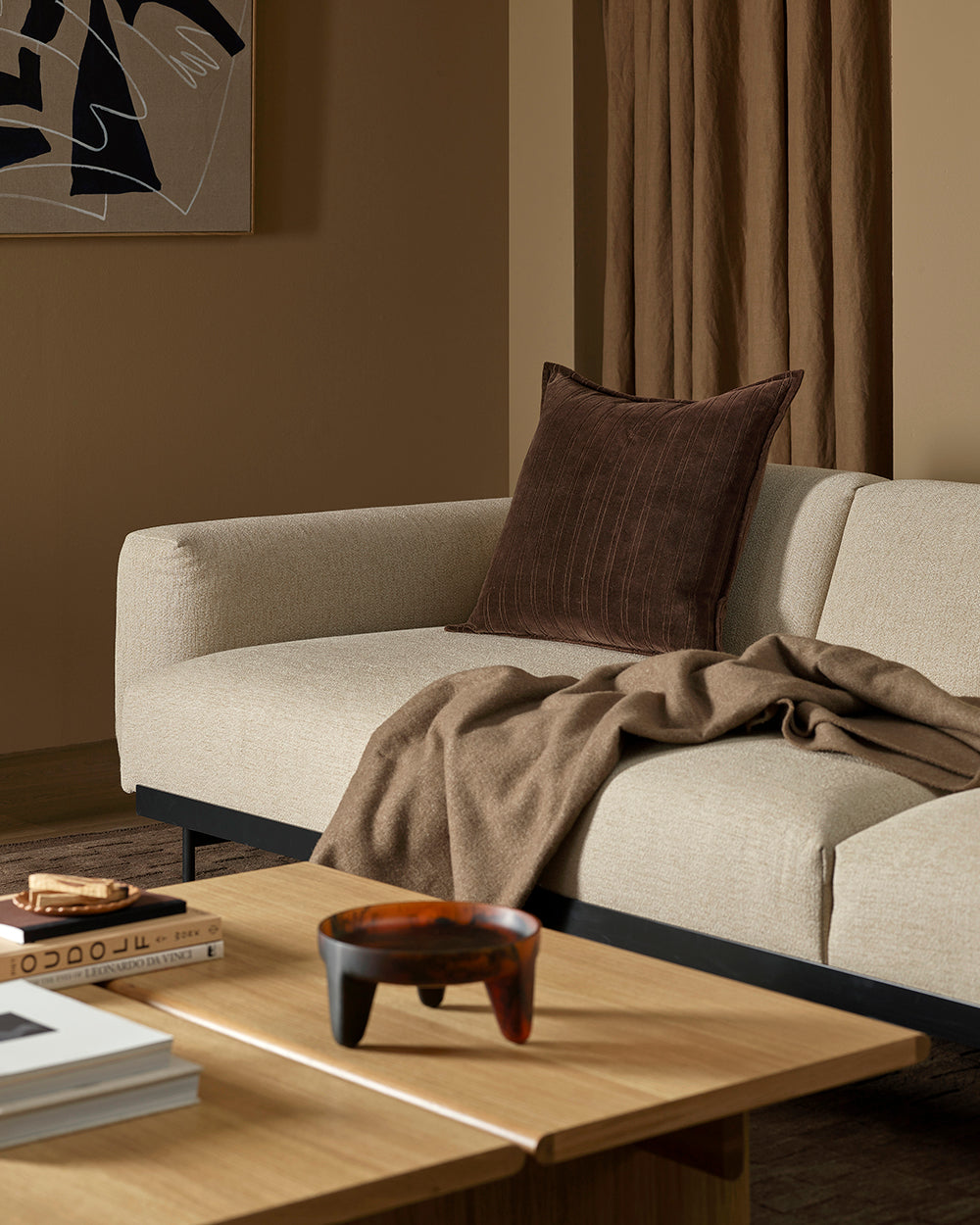 Beige sofa with a brown pillow and blanket in a living room setting.