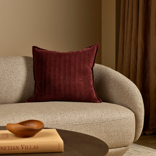 Gray sofa with a burgundy pillow and a wooden bowl on a book in a room with brown walls and curtains.
