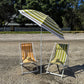 Two beach chairs under a striped umbrella on a gravel surface with trees in the background.