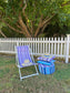 Outdoor setting with a striped deck chair, ottoman, and pillows against a white picket fence.
