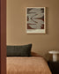 Framed artwork on a wall above a bed with a dark pillow.