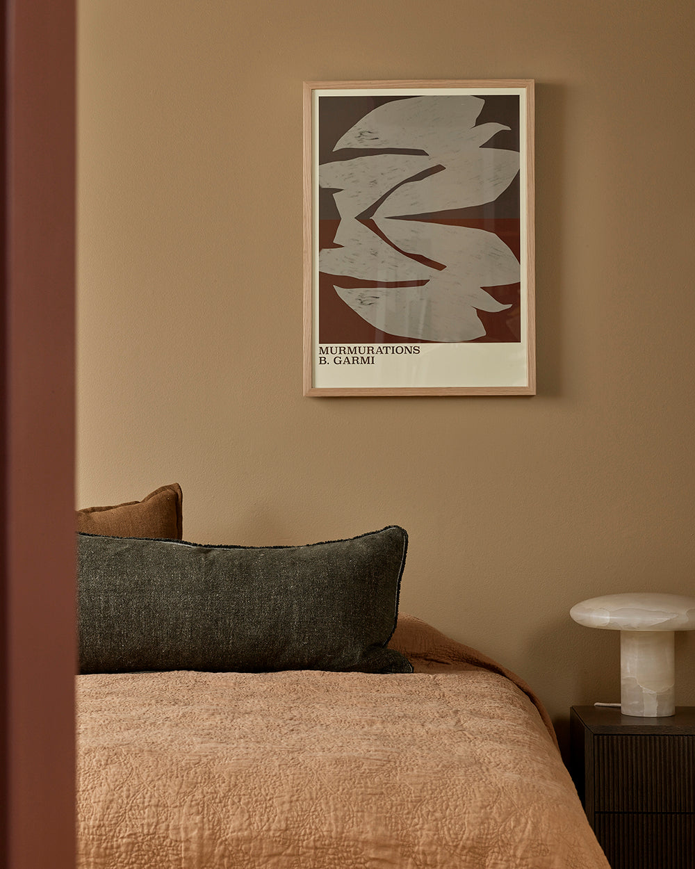 Framed abstract art on a wall above a bed with pillows and a nightstand.