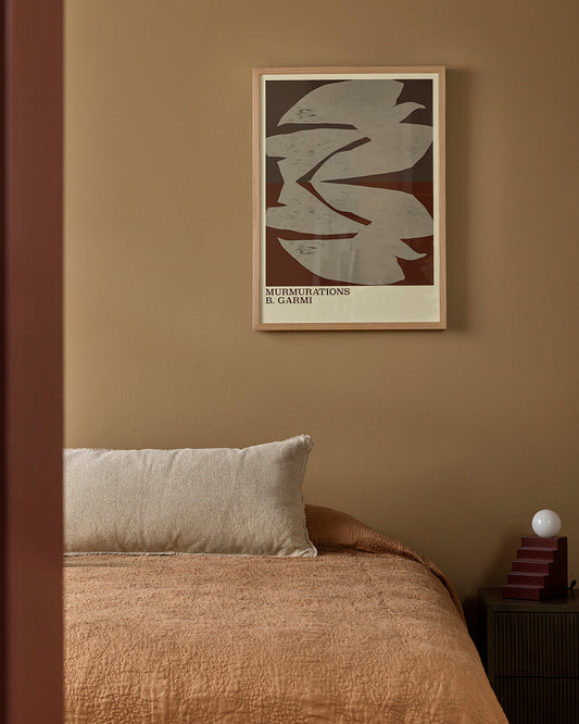 Framed artwork on a wall above a bed with a textured brown blanket.