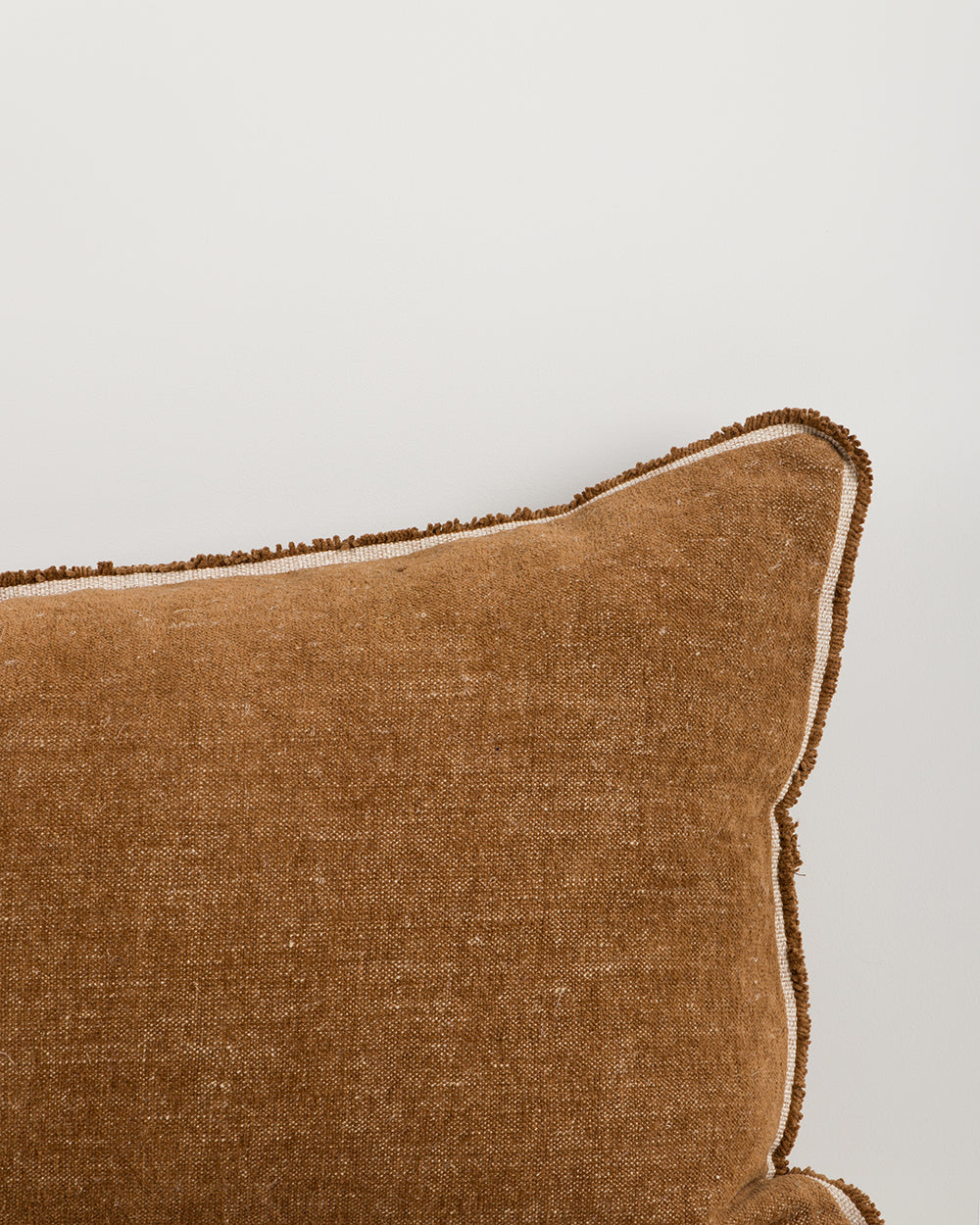 Brown textured pillow with decorative trim on a light gray background