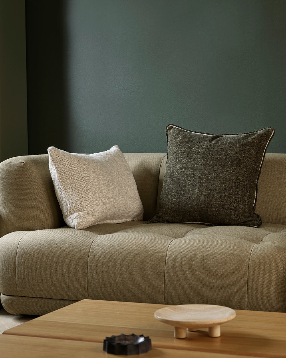 Beige sofa with two pillows against a dark wall, with a wooden coffee table in the foreground.