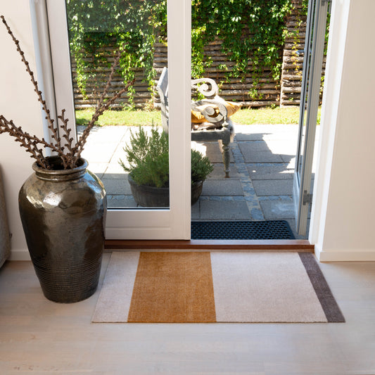 Decorative vase with branches on a rug in front of a glass door leading to a garden.
