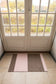 Rectangular rug with pink and brown stripes on a tiled floor in front of a glass door.