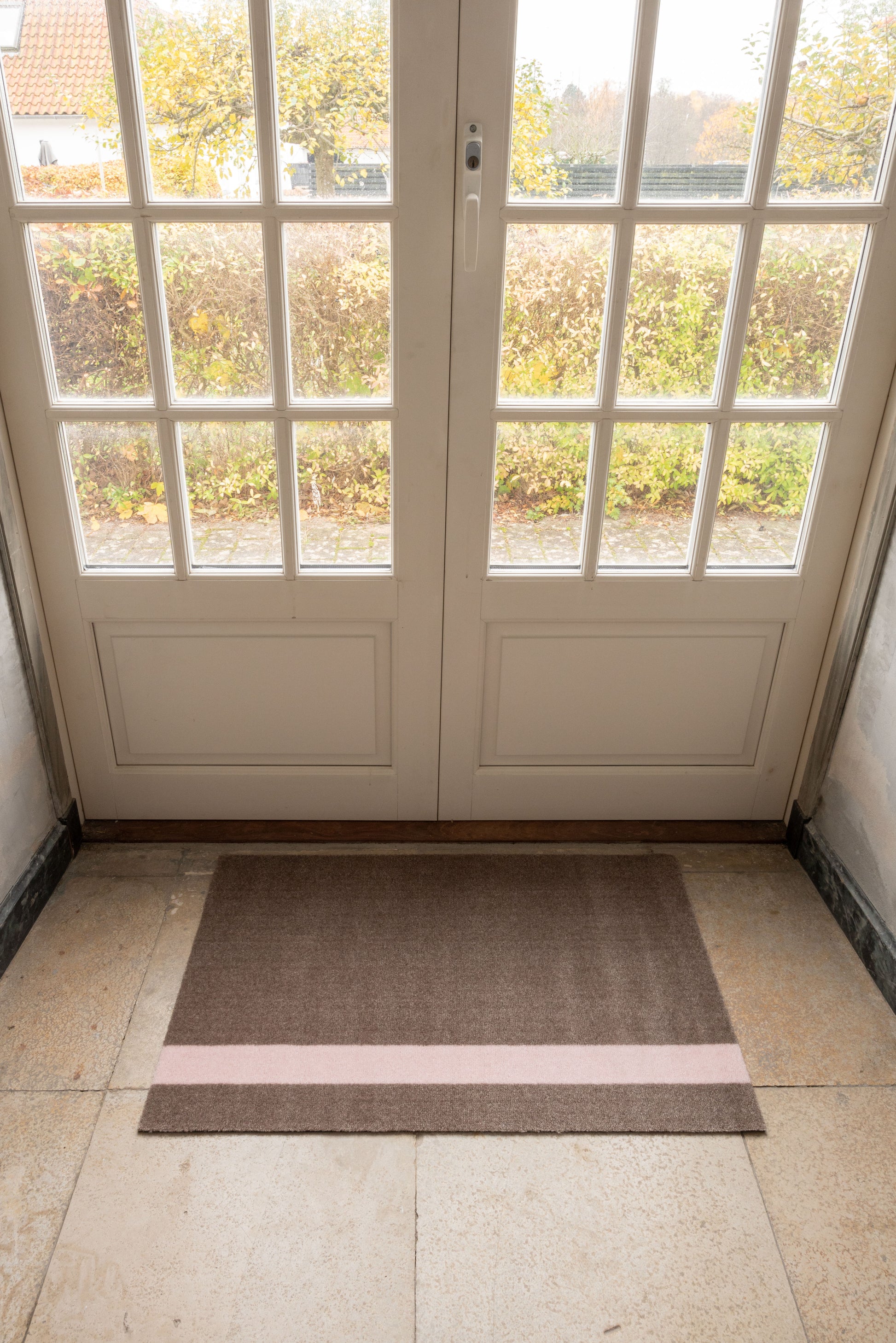 Brown doormat with a pink stripe in front of a glass door