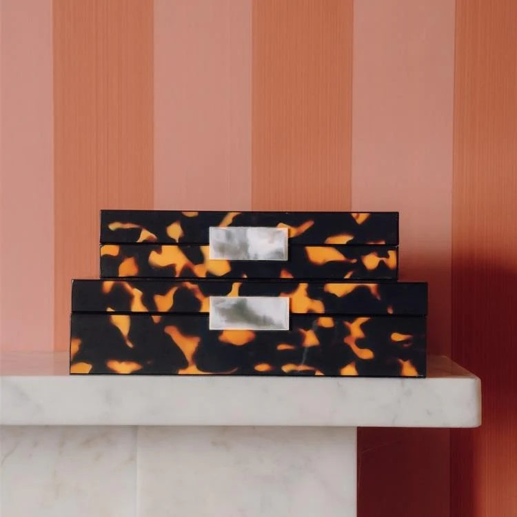 Set of tortoiseshell-patterned boxes on a marble surface with a striped wall background