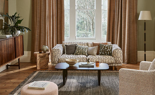 Living room with patterned sofa, wooden sideboard, and large window with curtains.