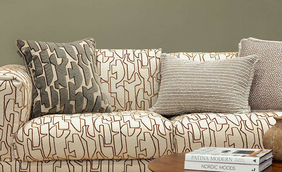 Patterned sofa with decorative pillows against a green wall