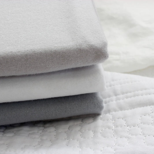 Stack of three sets of folded flannelette sheets in white, sage and slate