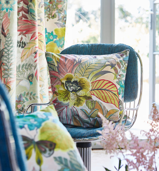 Botanist Fabric, large floral, leaves and fronds in yellows, green, pink, blue in a cushion on a blue fabric chair with wire stand. Matching curtain