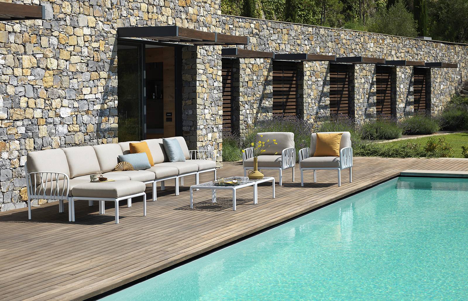 Komodo Outdoor Chair, white frame, grey cushion around the pool by a stonen wall