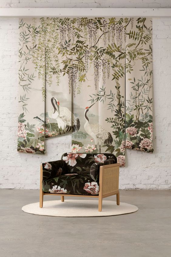 Mizu garden fabric panel from mokum featuring 2 cranes, pink peonies, wisteria and green bamboo and foliage in a serene water garden on fabric wall panels with a black and pink floral wooden chair in front, white brick walls, grey carpet and chair on small white rug