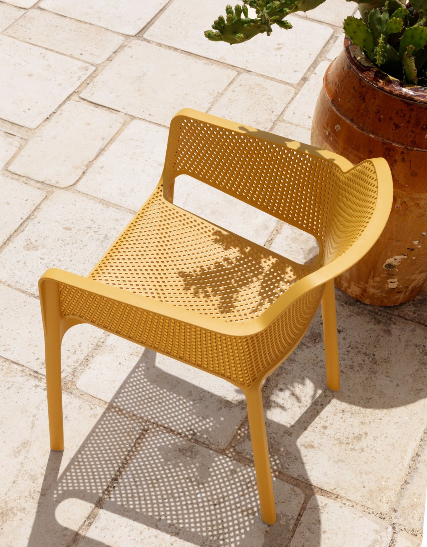 nardi net chair in mustard on a patio with white flag stones beside a rustic red plant pot and cactus