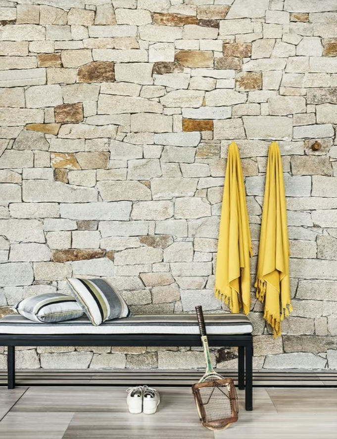 south beach strip fabric in charcoal on two cushions sitting on a bench with black legs in the same fabric against a stone wall with 2 yellow towels hanging up on