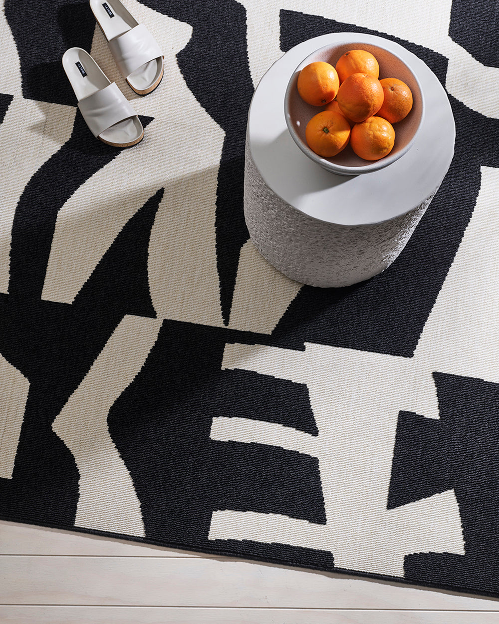 copacabana black and ecru rug with slide shoes and a bowl of oranges on a stone stool