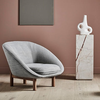 elle block marble plinth with a white vase on top and a tolv grey fabric chair with wooden legs. Pale wooden floors and blush pink walls