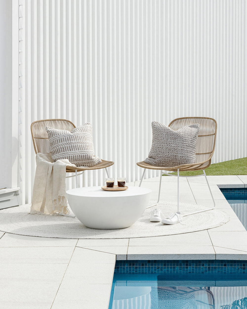 Elton Wicker outdoor cushion with the morgan cushion on wicker chairs beside a pool surrounded by white tiles