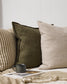 Flaxmill linen cushions in olive with two other matching plain and striped cushions on a sofa with a cup of coffee on a magazine and throw in front