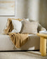 Keaton Linen cushion in cream on couch with textured beige cushion and taupe throw on a ivory couch in a lifestyle scene with little patterned cream wall paper and painting