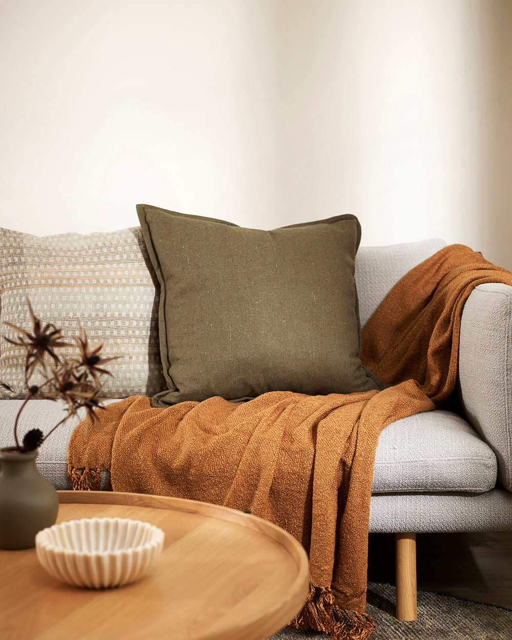 Maximum felt khaki cushion on a grey sofa with a rust coloured throw and textured beige cushion alongside