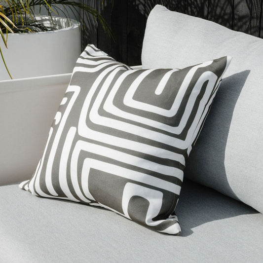 Pico outdoor cushion with deep olive tribal lines on white background placed on a grey outdoor chair with concrete plant pot with fern in the background