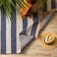 Summit outdoor rug with blue stripes on wooden floor with a rattan hat and bag