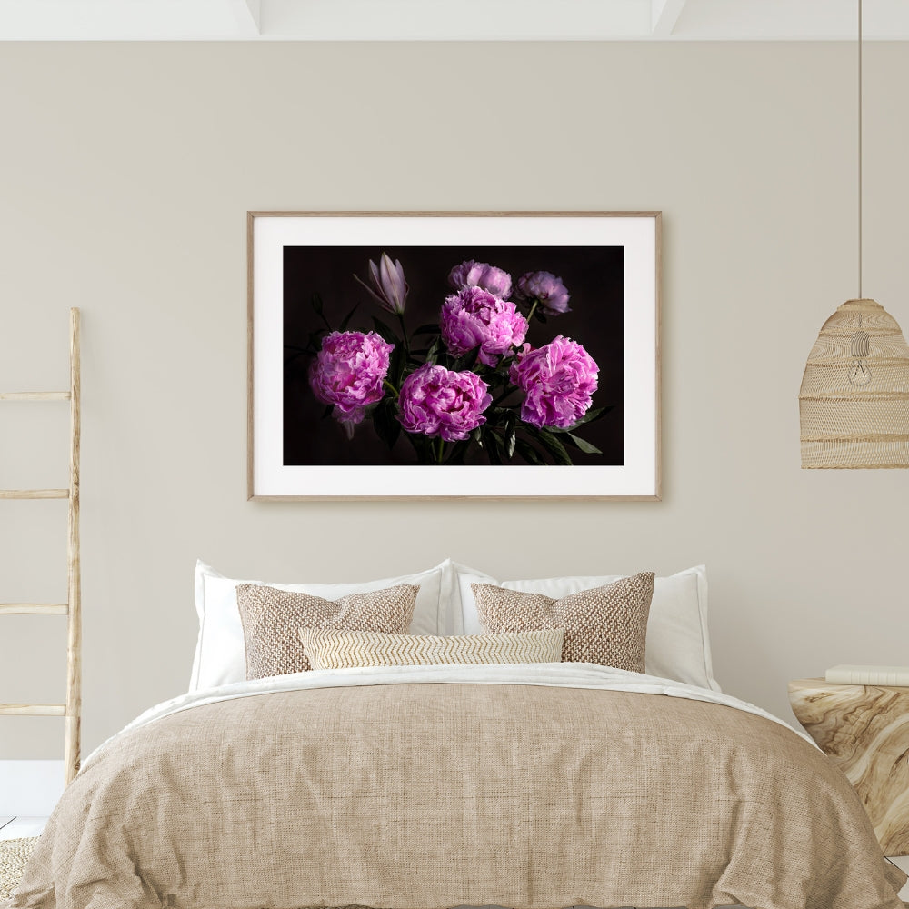 pink peonies on a black ground in a framed picture above a beige and white bed with grey walls and a rattan light shade and wooden ladder