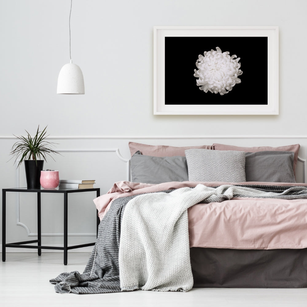 white chrysanthemum on a black background in a white bedroom with pink and grey bed linen and cushions, black metal side table with pink and black objects