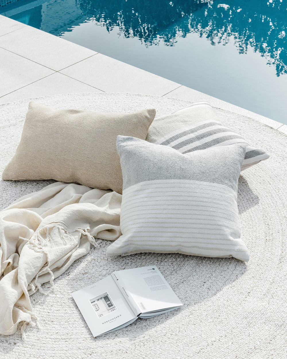 Willett outdoor cushion with the verdi on a mat beside the pool